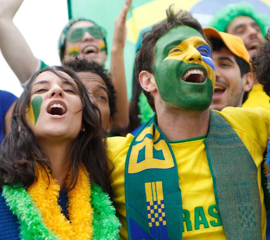 Foto de homem com maquiagem de bandeira do Brasil e outras pessoas vestidas de verde e amarelo.