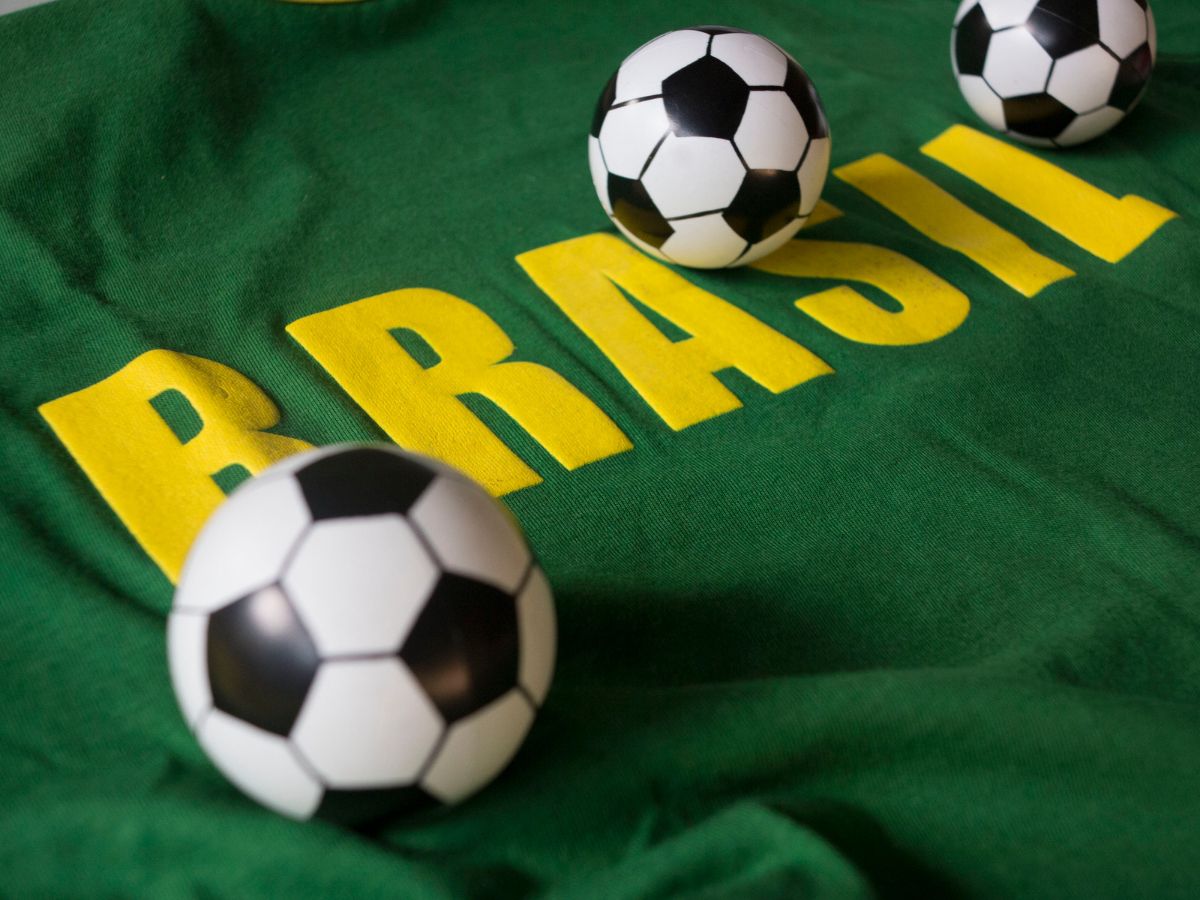 Imagem de tecido verde escrito "Brasil" de amarelo com bolas de futebol em cima.