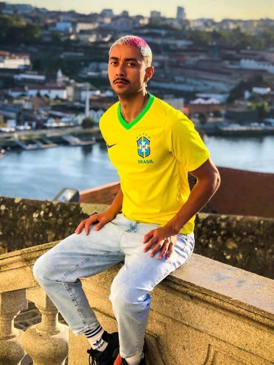Imagem de homem sentado em corrimão de pedra de escada, usando camiseta amarela do Brasil + calça jeans + tênis preto - looks masculinos para a Copa do Mundo.