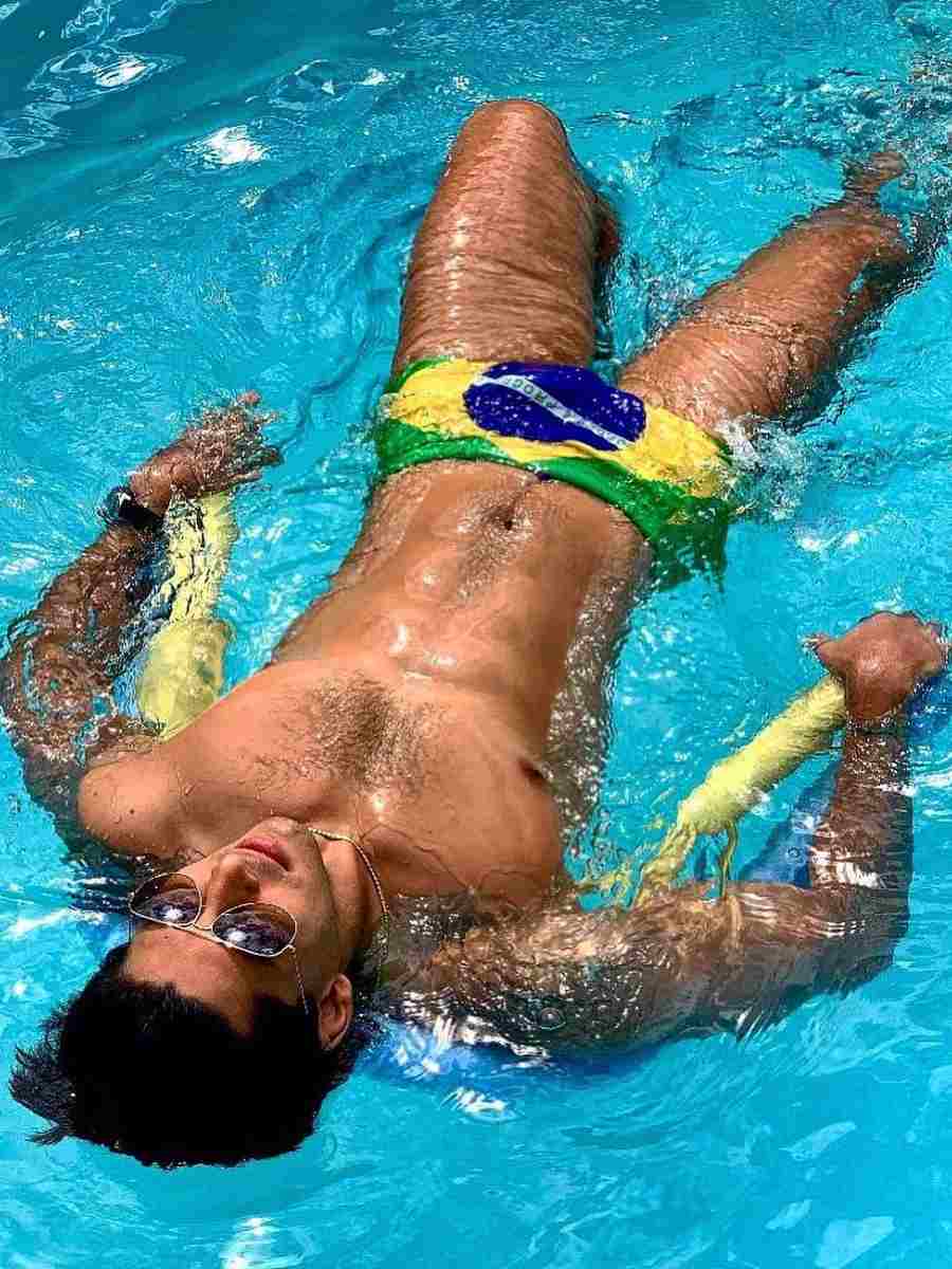 Imagem com fundo água de piscina. No centro, homem boiando usando sunga de bandeira do Brasil.