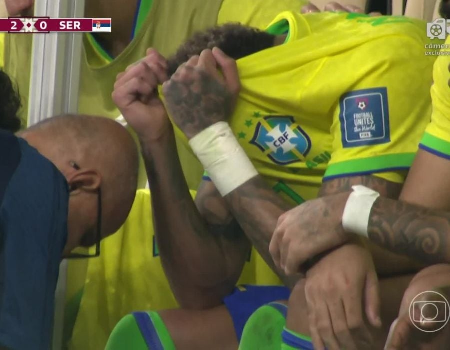 Neymar escondendo o rosto no uniforme enquanto é atendido por médicos