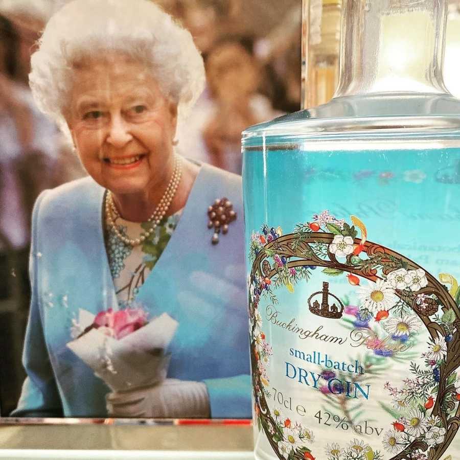 Imagem de garrafa de Buckingham Palace Gin, da Rainha Elizabeth II, com foto dela ao lado.
