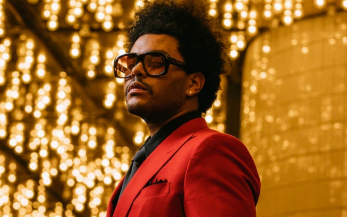 Foto do cantor The Weeknd com terno vermelho e fundo dourado