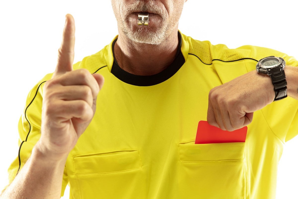 árbitro de amarelo, segurando um cartão vermelho no bolso da blusa e usando um apito
