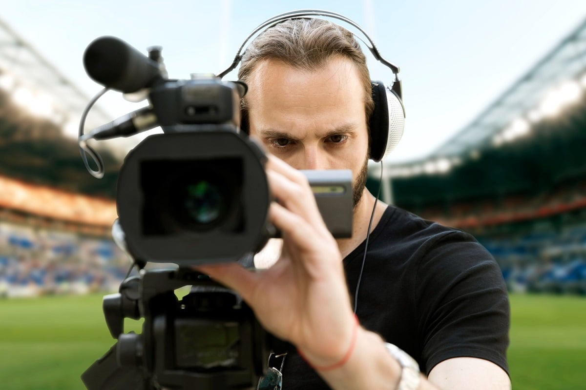 homem segurando uma câmera, filmando dentro de um campo de futebol