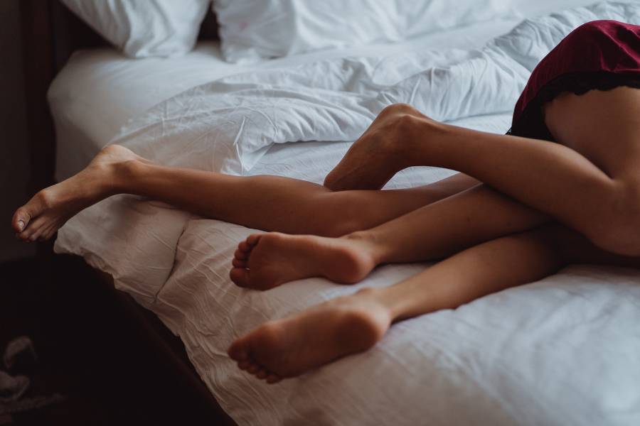 Duas mulheres abraçadas na cama. Na foto, só é possível ver as pernas do casal