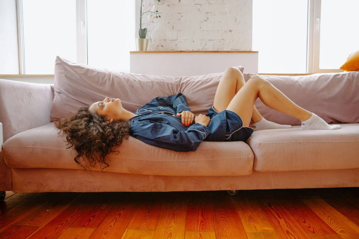 mulher com cólica menstrual usando pijama e deitada no sofá