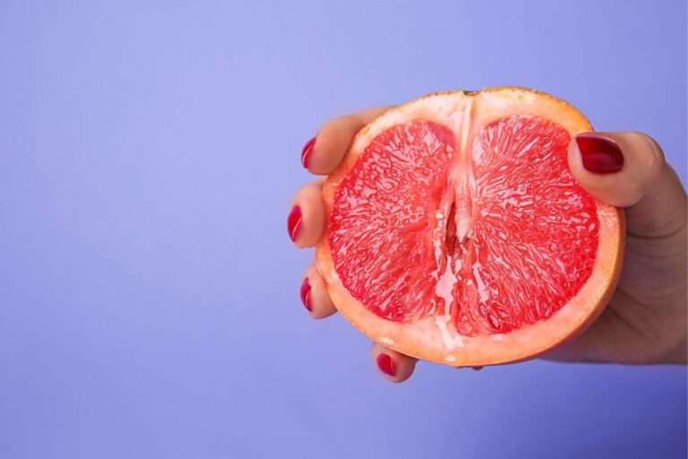 Fundo roxo com mão de mulher segurando uma toranja, simbolizando o pompoarismo