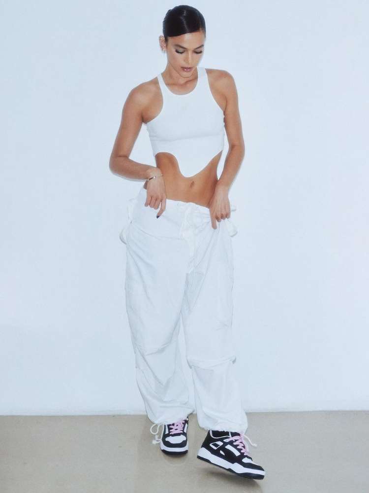 Foto de Bruna Marquezine usando tendências Verão 2023: cropped branco com recortes, calça parachute branca e tênis Puma