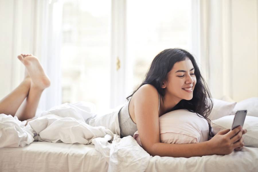 mulher deitada na cama praticando sexting para apimentar a relação