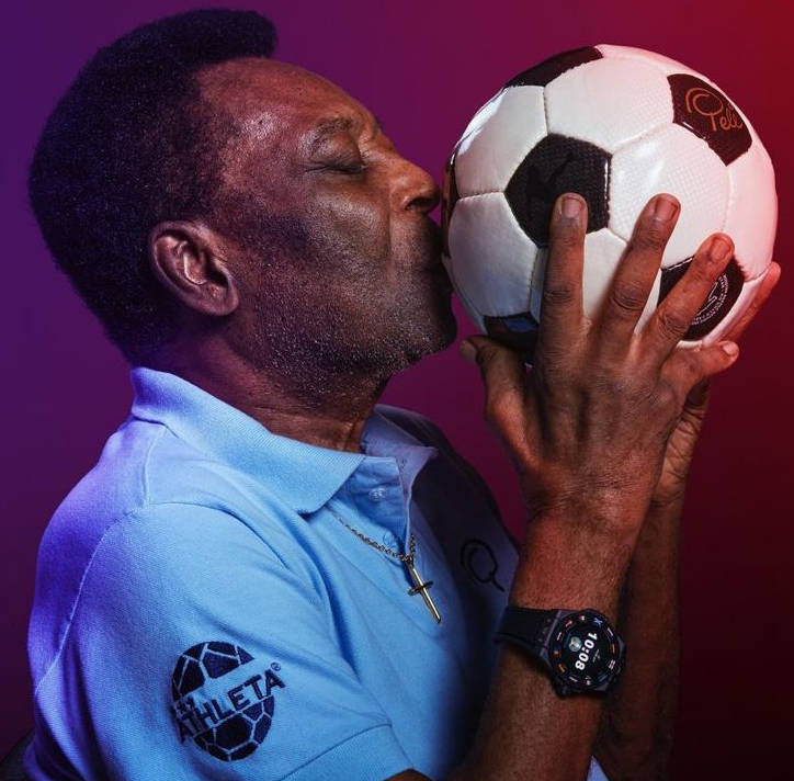 Pelé e beijando uma bola de futebol com camisa azul