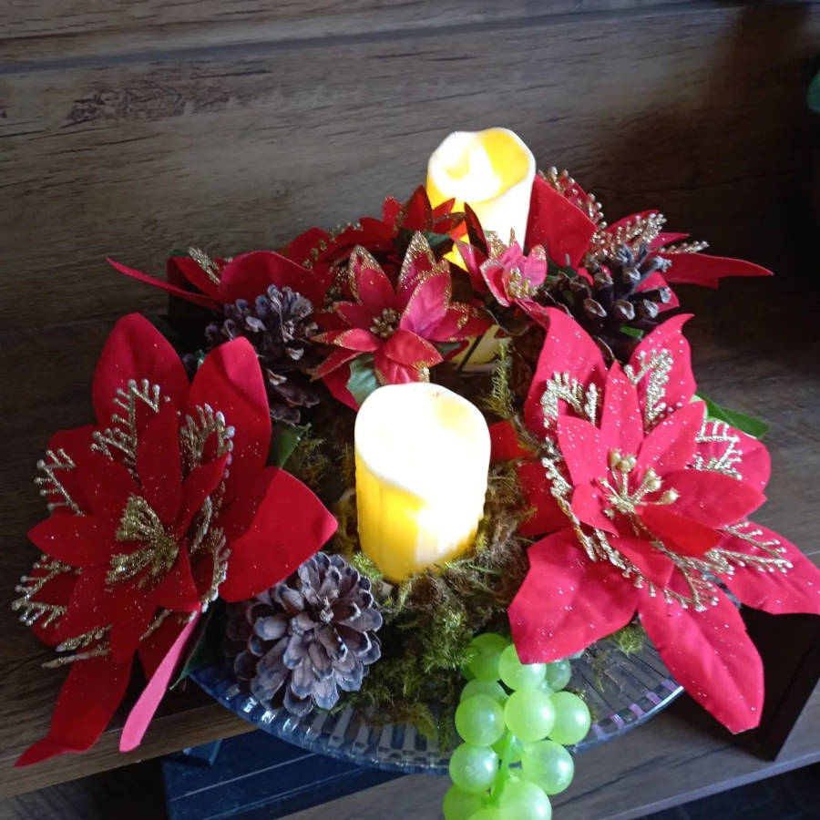 Arranjo de mesa de Natal redondo com flores, velas e uvas.