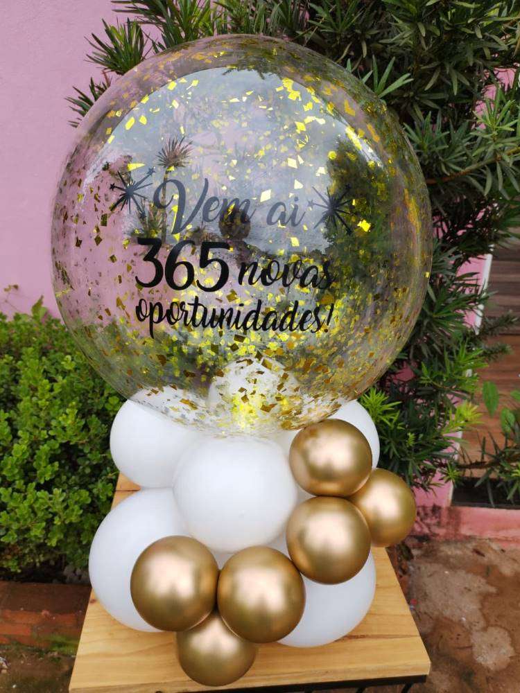 Balão grande e transparente com mensagem de "Vem aí 365 novas oportunidades" e balões brancos e dourados. 