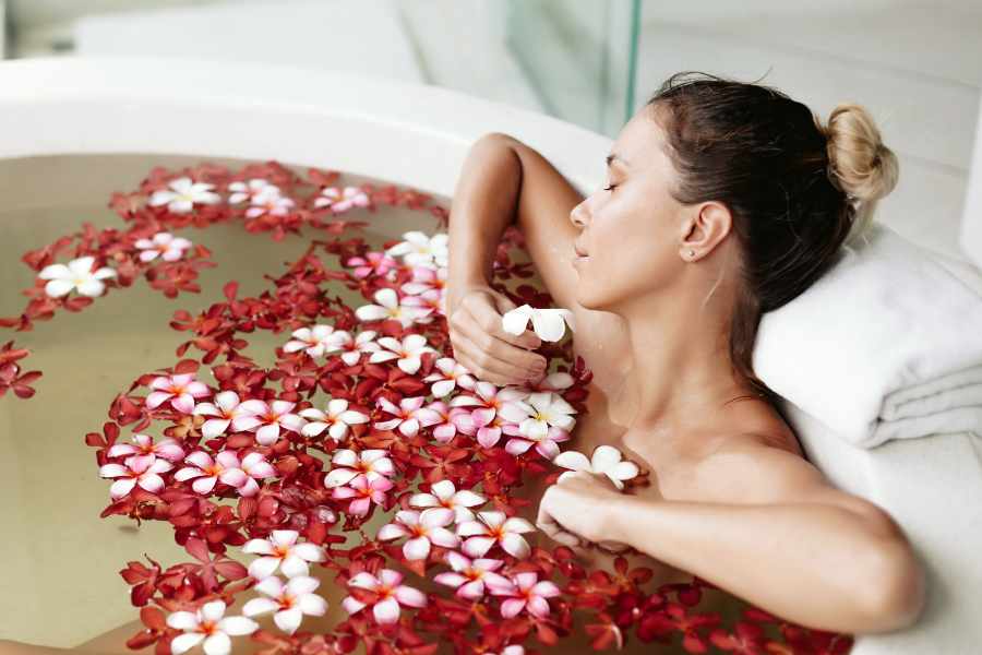 Mulher tomando banho de ervas para tirar energias negativas na banheira com flores.