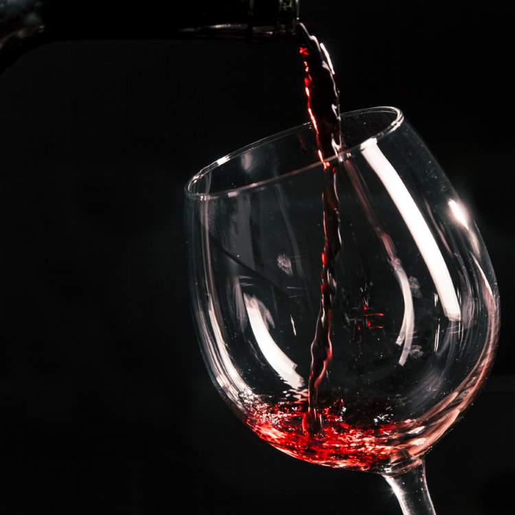Taça de vidro com vinho sendo derramado. 