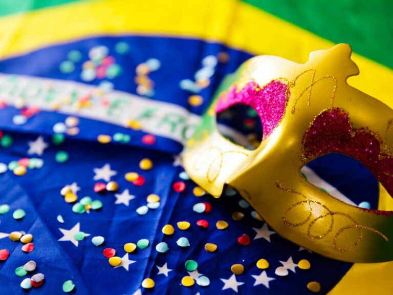 Foto de bandeira do Brasil com máscara de Carnaval e confetes jogados.