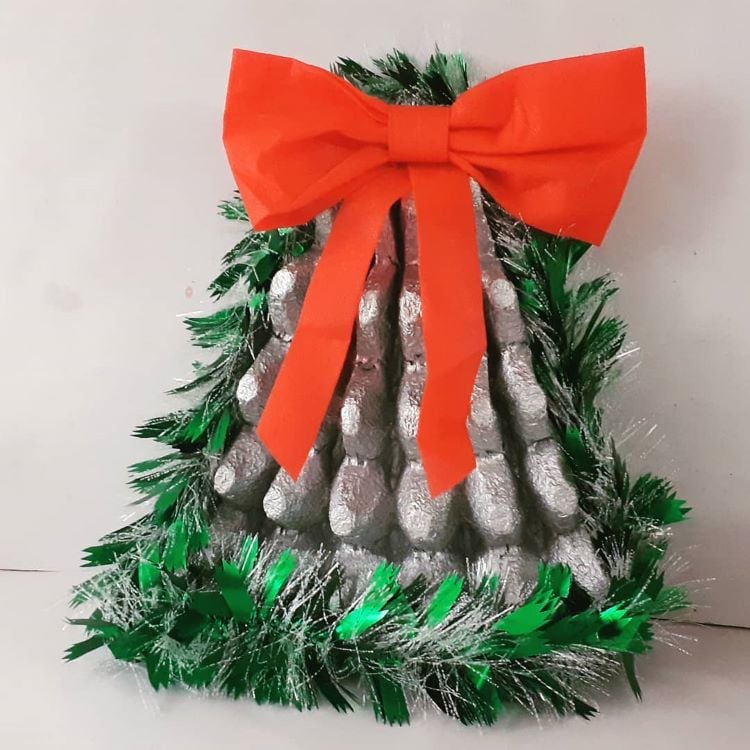 Sino natalino feito com caixa de ovo pintada de prata, festão e fita verdes e laço vermelho.
