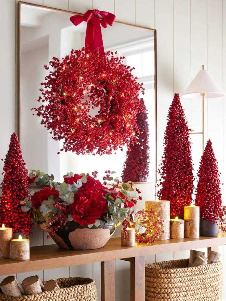 Aparador com pequenas árvores natalinas em vermelho, flores e guirlanda vermelha pendurada. 