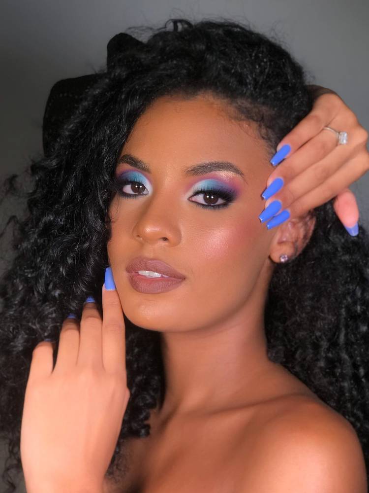Mulher de pele negra com make azul nos olhos, pele glow e batom nude.