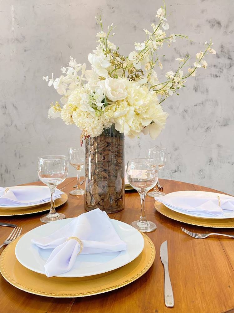 Arranjo de flores brancas em mesa posta com pratos brancos e sousplat