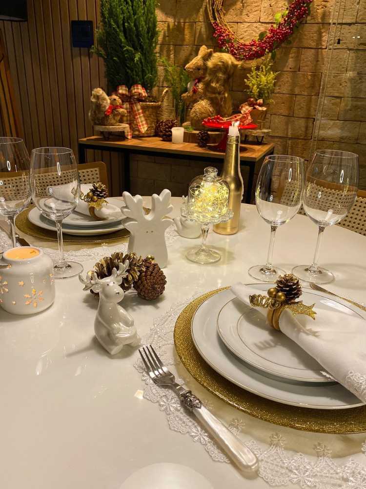 Mesa posta com enfeites natalinos, sousplat dourado com pratos brancos. 