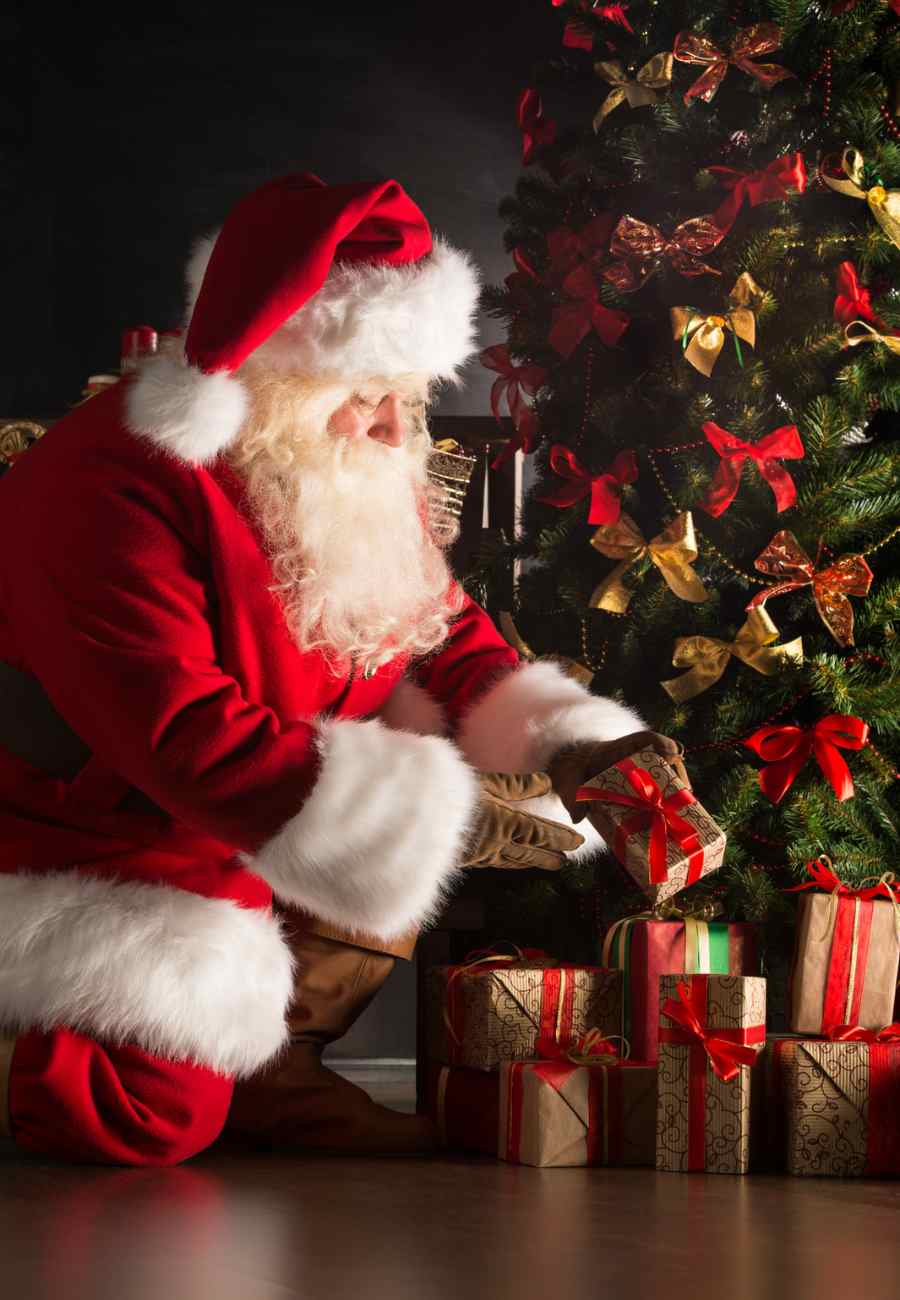 Foto de Papai Noel colocando presente debaixo da árvore de Natal.
