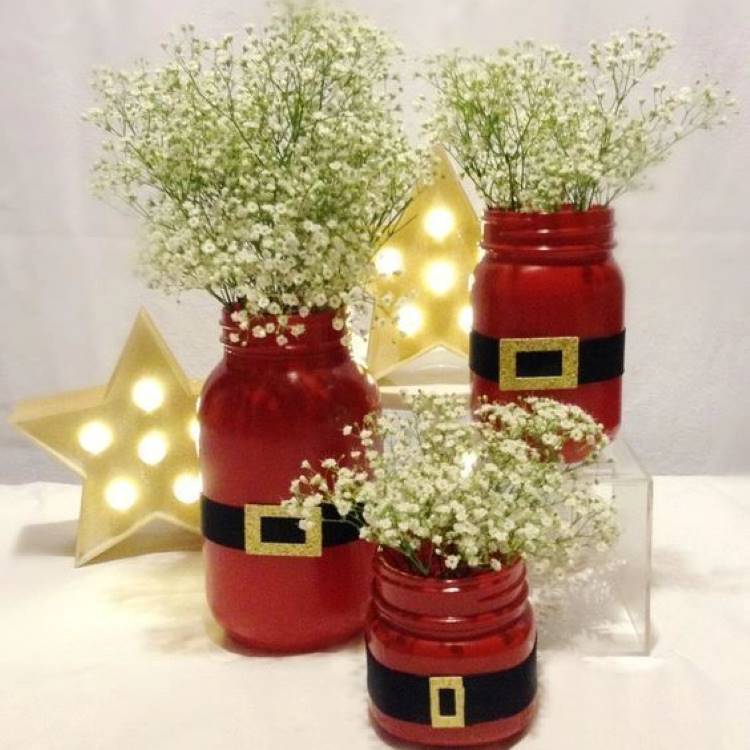 Três potes de vidro pintados de vermelho e com cinto do Papai Noel com plantinhas dentro.