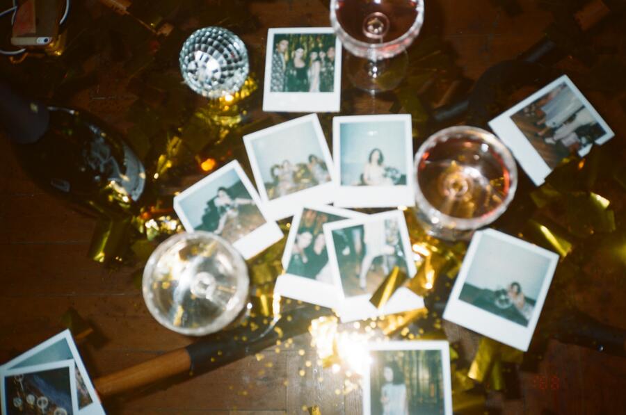 copos com bebida, fotos polaroid e um mini globo de festa em cima de uma mesa de madeira