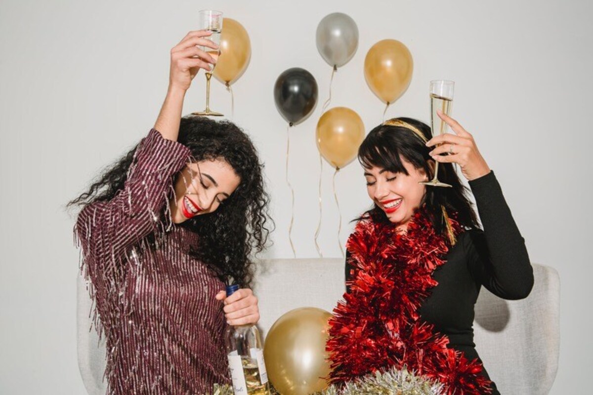 duas mulheres com copos de bebida nas mãos festejando com balões ao redor