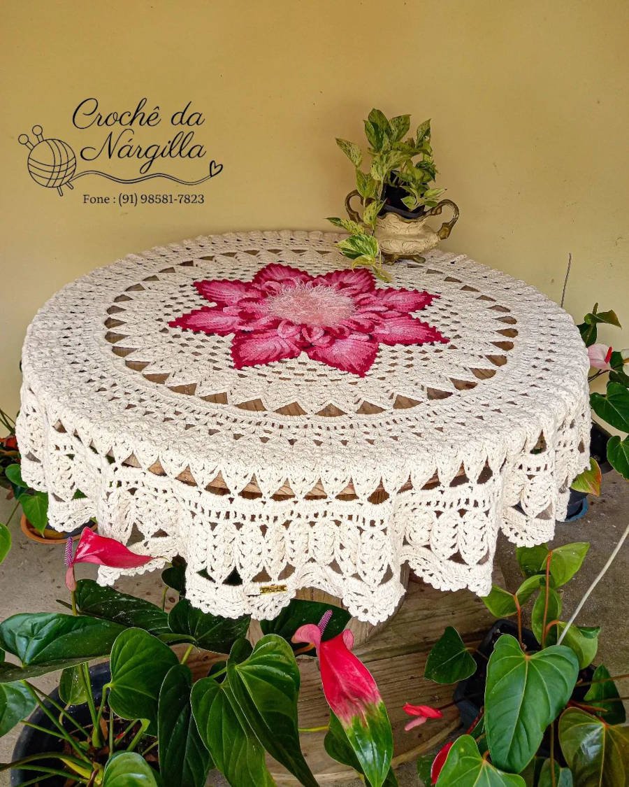Toalha de mesa de crochê com grande flor rosa no centro.
