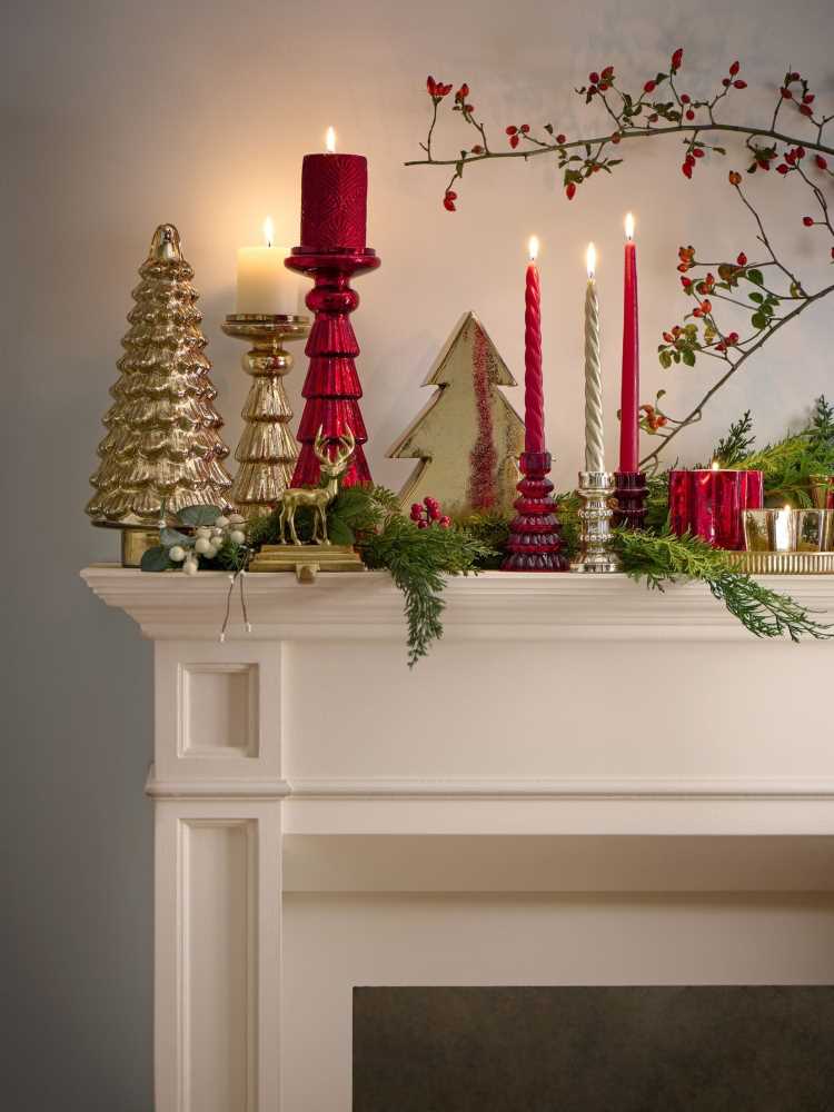 Aparador branco com pequenas árvores natalinas, muitas plantinhas e velas vermelhas. 