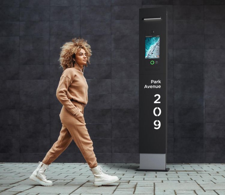 mulher andando na rua ao lado de um totem de interfone IP