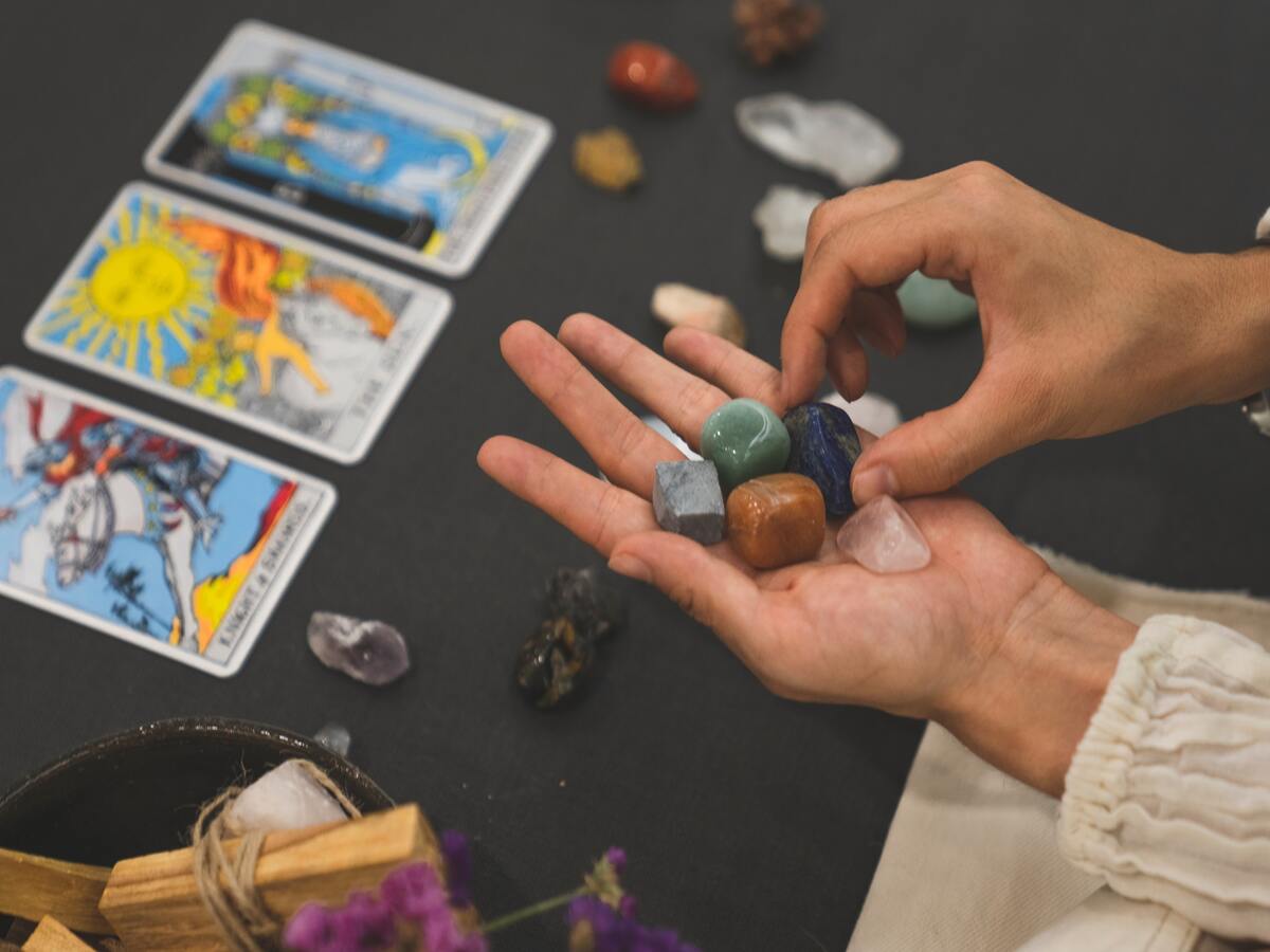 Imagem de uma mão feminina segurando cristais em frente a uma mesa com 3 cartas de tarot abertas