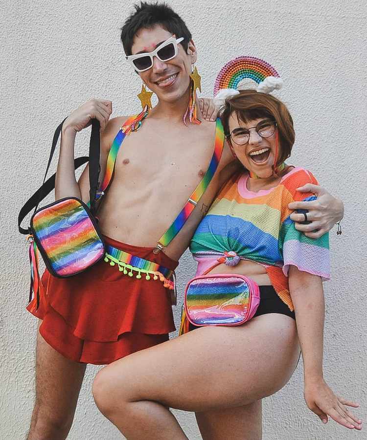 Homem e mulher com look e pochetes cores da bandeira LGBTQIA+ para o Carnaval.