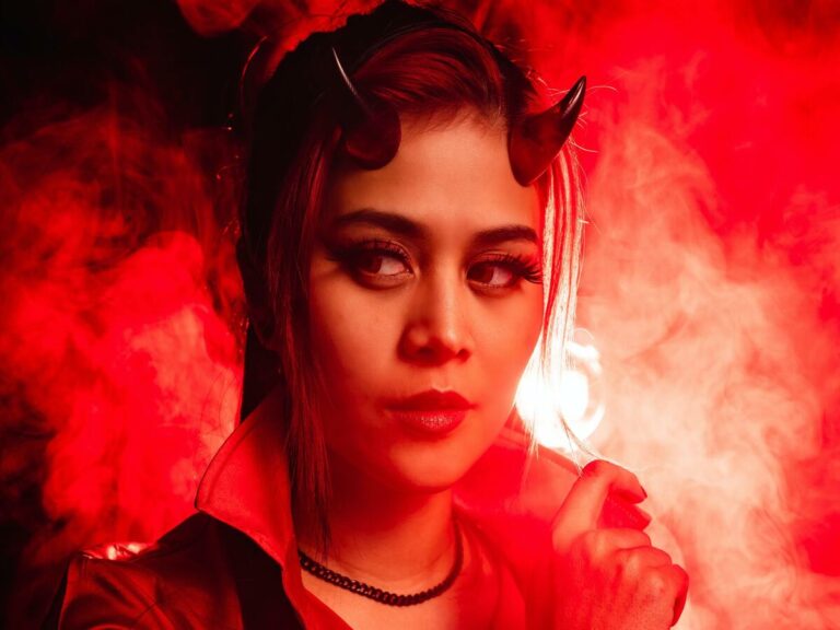 mulher com chifres, parecendo o diabo, com uma fumaça e luzes vermelhas em volta para representar o lado sombrio de cada signo