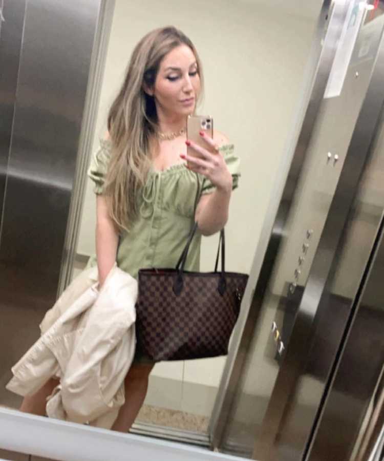 Selfie da sister em espelho de elevador, ela usa vestido, segura casado e bolsa.