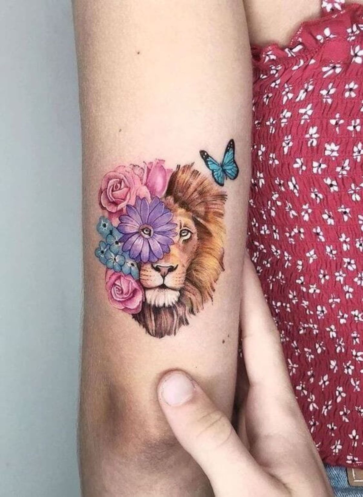Tatuagem de leão colorida com flores rosa e roxa ao redor