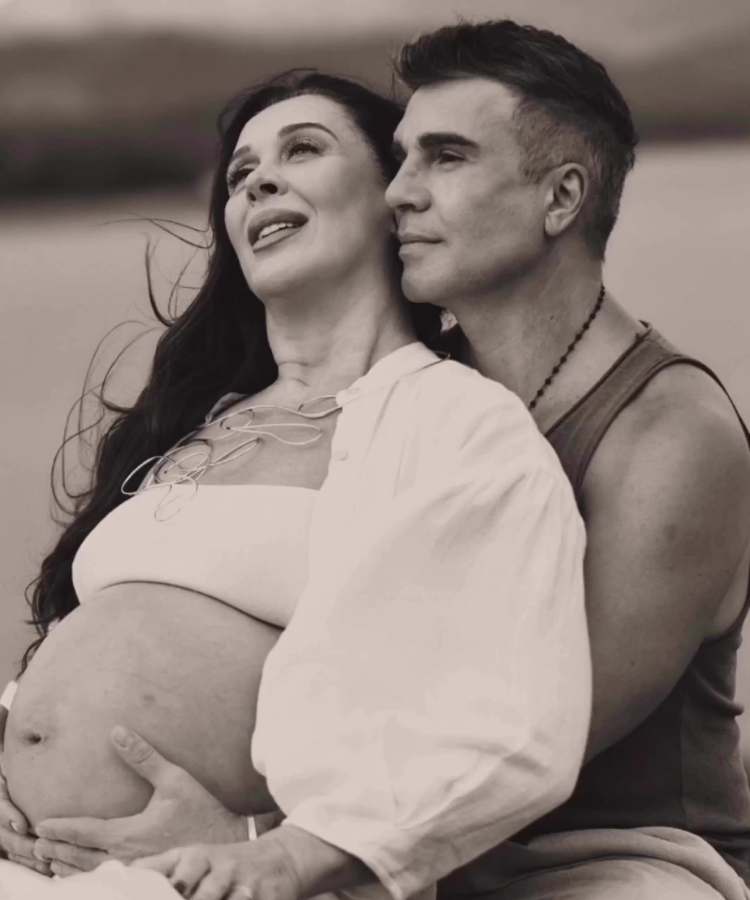 Atriz Claudia Raia grávida e o esposo Jarbas de Mello, abraçados com ele com a mão em sua barriga. 
