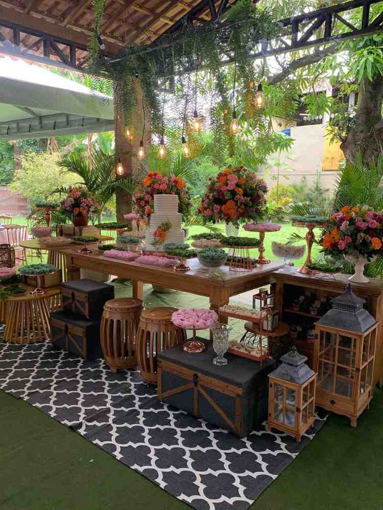 Decoração de mesa de bolo casamento rústica com malas, lanternas e flores coloridas.