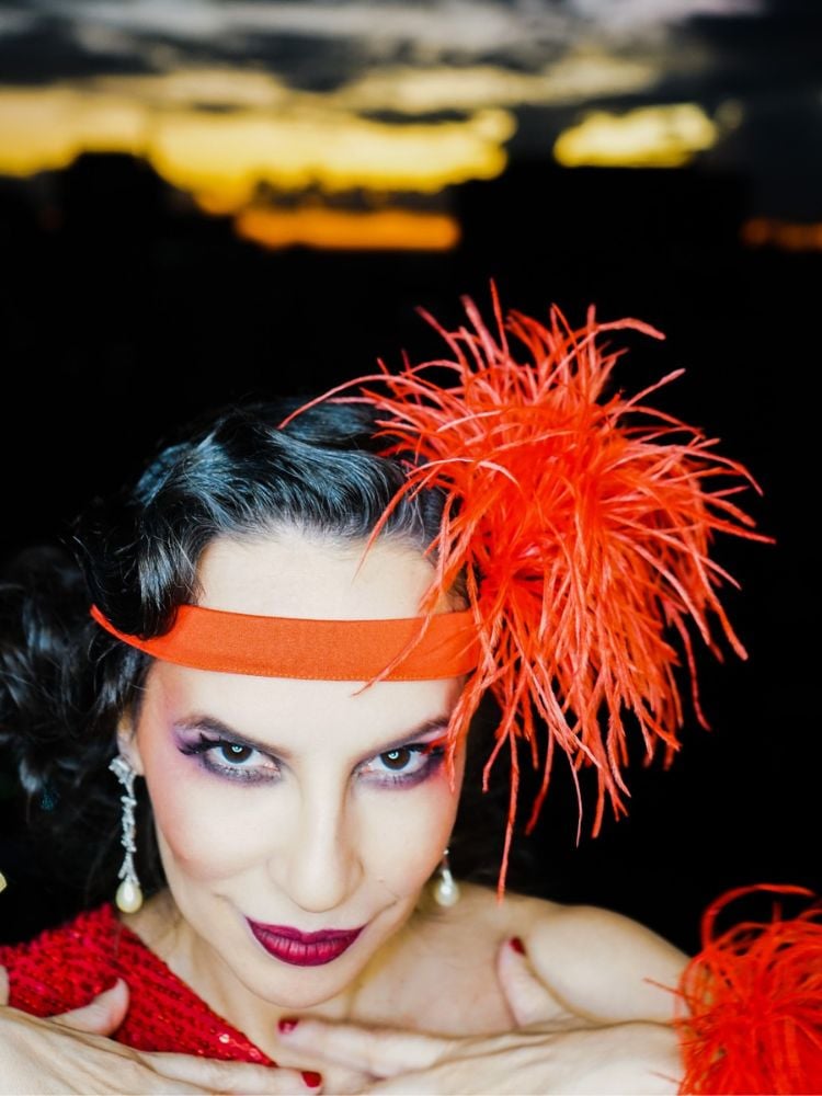 na foto, close de Denise Pitta, utilizando acessórios laranja e maquiagem. 