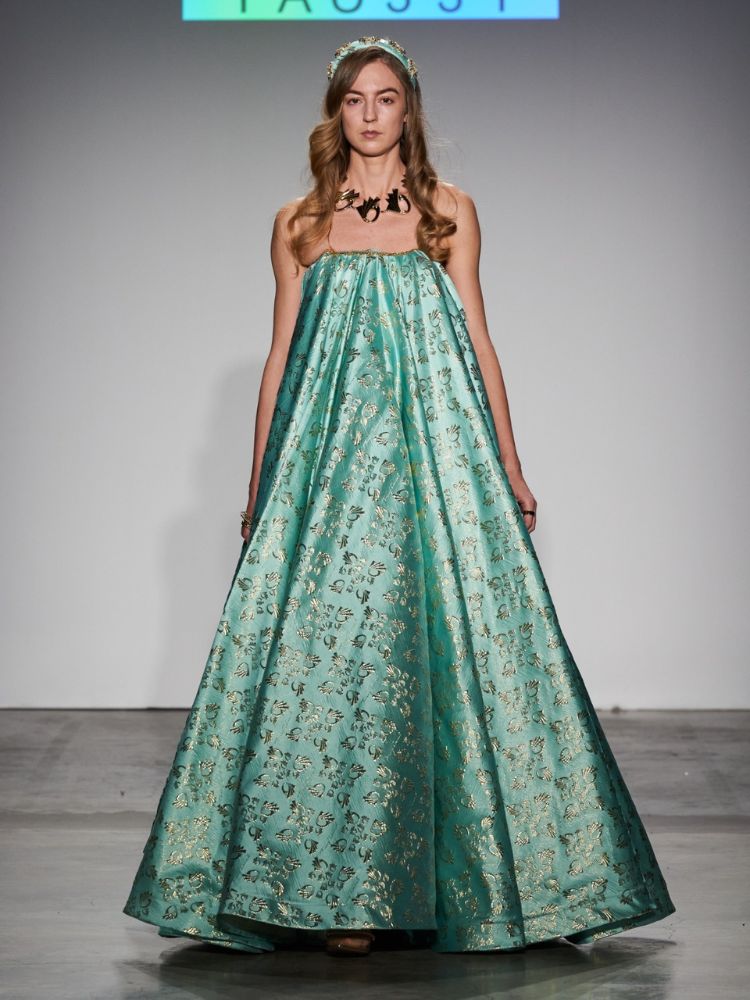 modelo usando vestido longo, verde e florido, com colar dourado e tiara. 