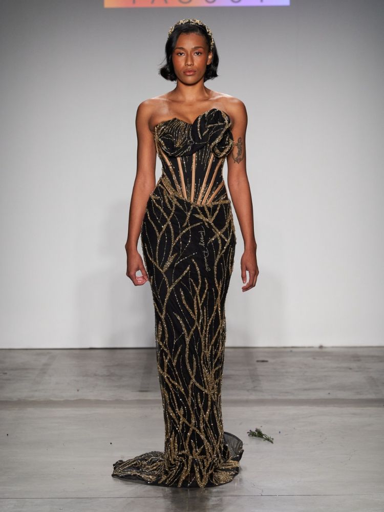 modelo com vestido longo preto com detalhes dourados, tiara e cabelos curtos. 