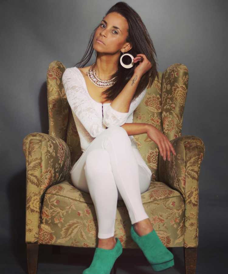 Domitila do Big Brother Brasil 2023 de cabelo liso em foto usando roupa branca, saltos verdes e sentada em poltrona.