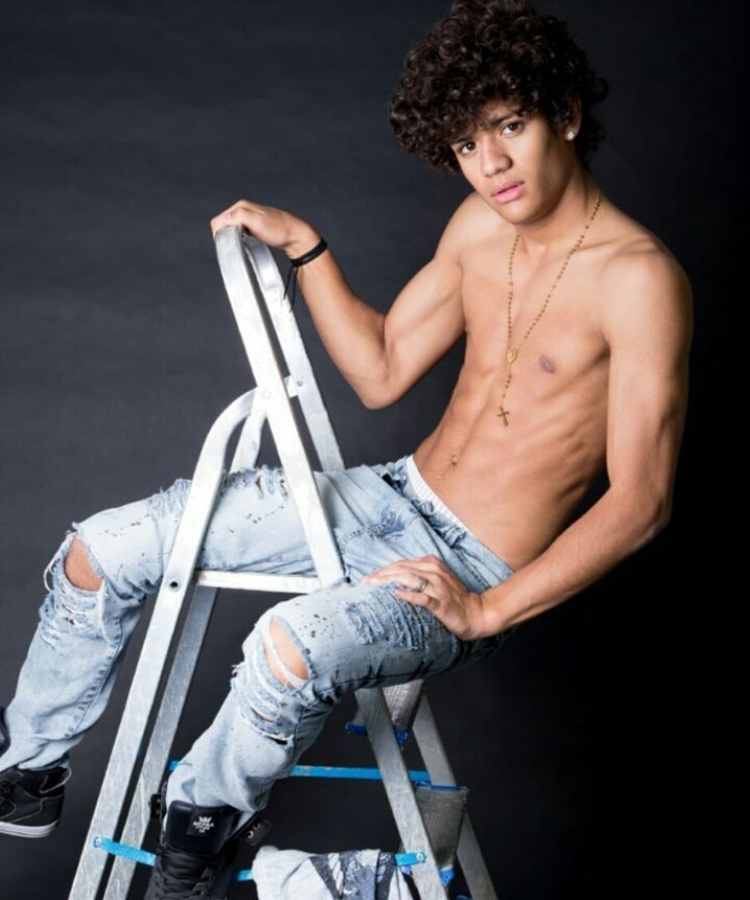 Gabriel Santana do BBB 23 aos 16 anos sentado em escada, sem camisa e de calça jeans.