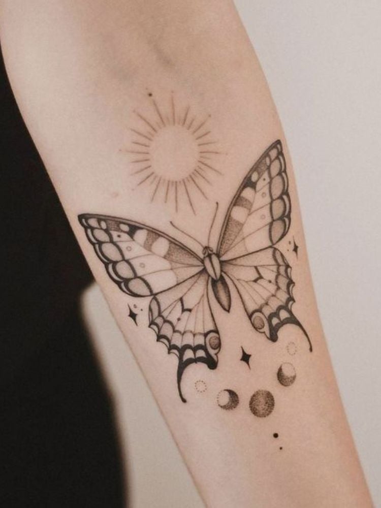 Foto de tatuagem de borboleta, com sol e fazes da lua no antebraço.