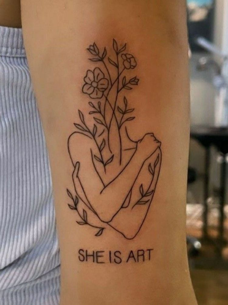 tatuagem no braço com a frase "she is art" e um tronco se abraçando. 