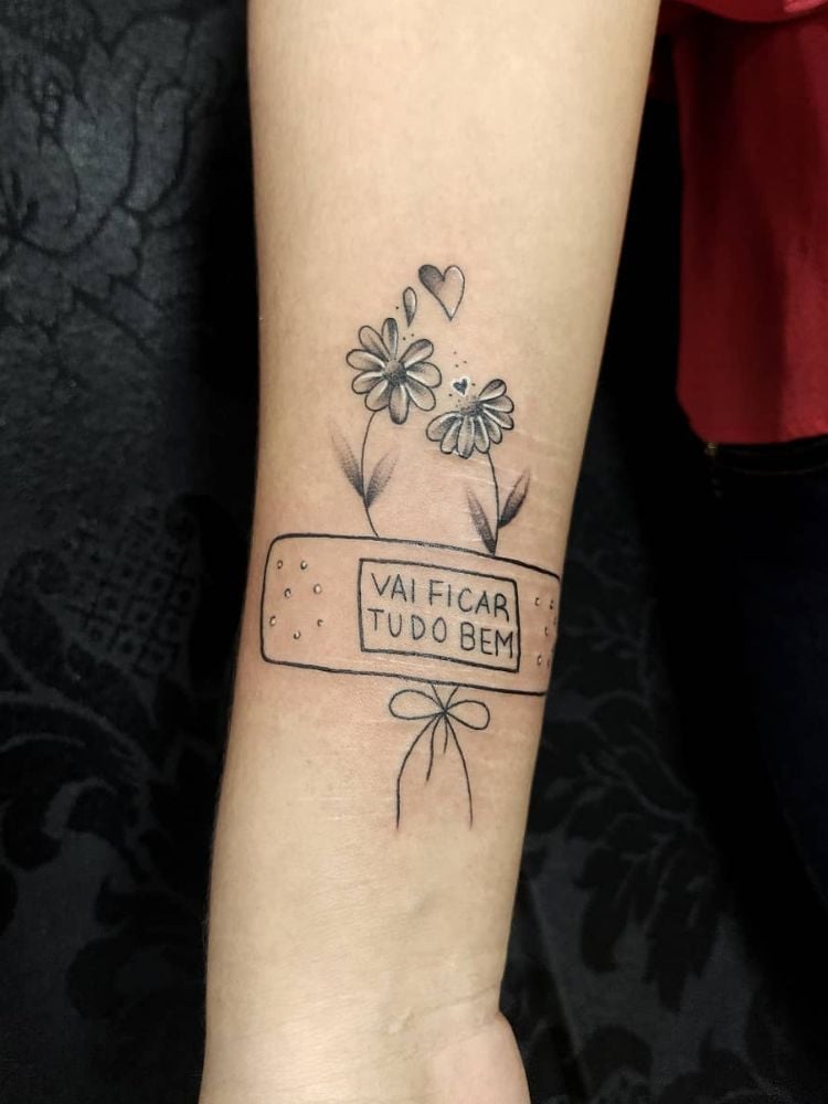 tatuagem com a frase "vai ficar tudo bem" e flores. 