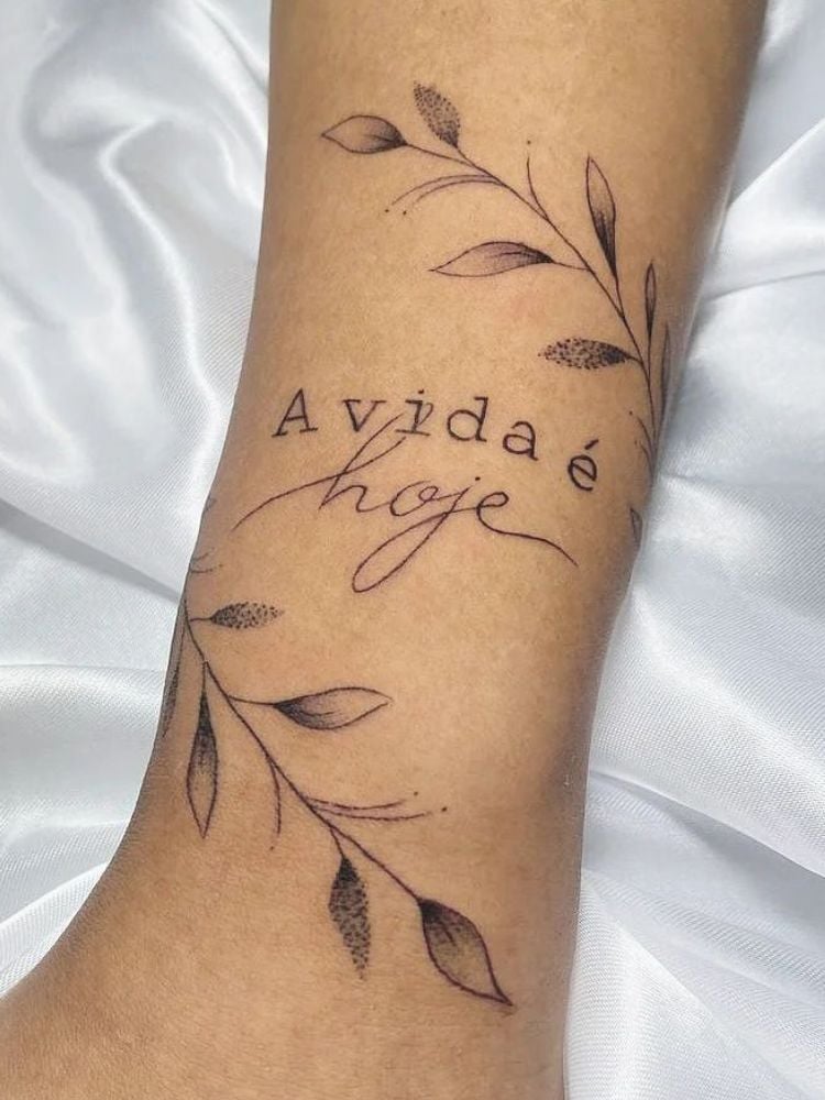 tatuagem com a frase "a vida é hoje" e um ramo de planta. 