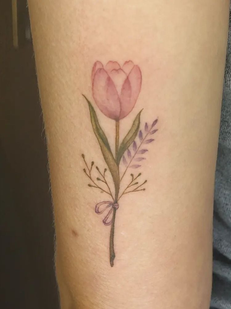 Foto de tatuagem no braço, com tulipa rosa e um ramo roxo.