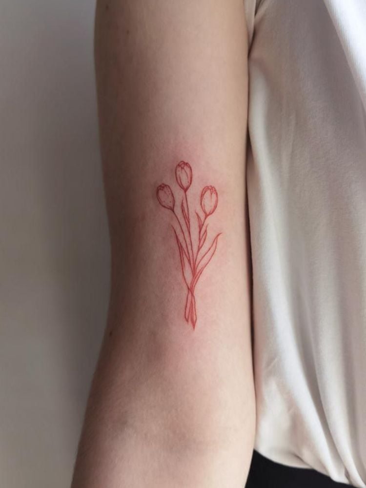 Foto de tatuagem no bíceps, com três tulipas em traço vermelho.